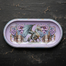 Load image into Gallery viewer, An oval decorative tray featuring a pastel illustration of a green dragon with purple flowers and ornate gold details on a light pink background, set against a dark textured surface.